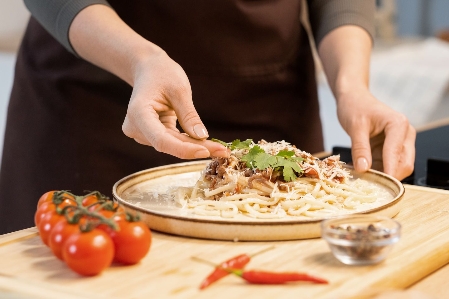 Hands of female decorating top of boiled homemade spaghetti with parsley leaves while standing by kitchen table