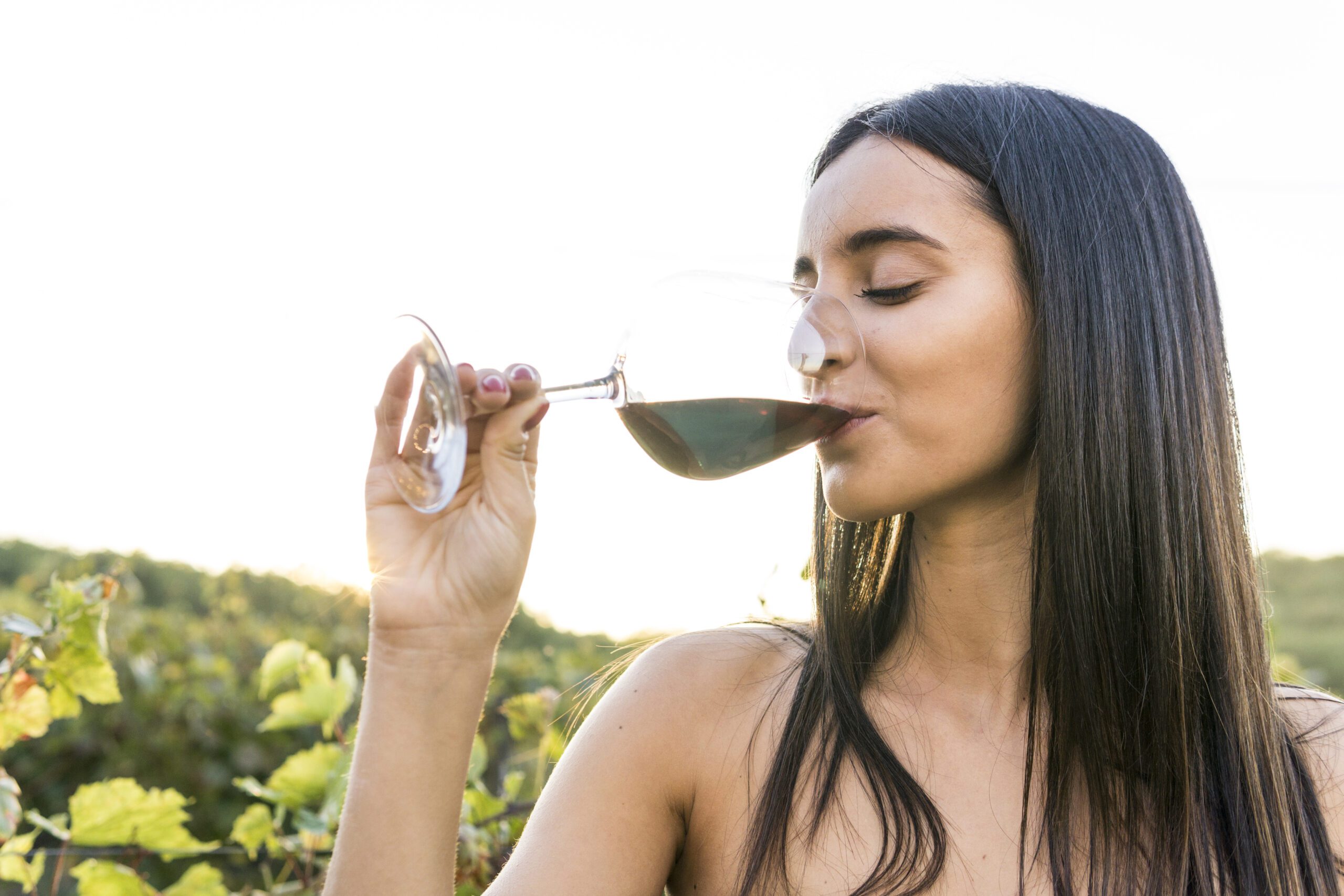 Italy, Tuscany, Siena, young woman drinking red wine in a vineyard at sunset