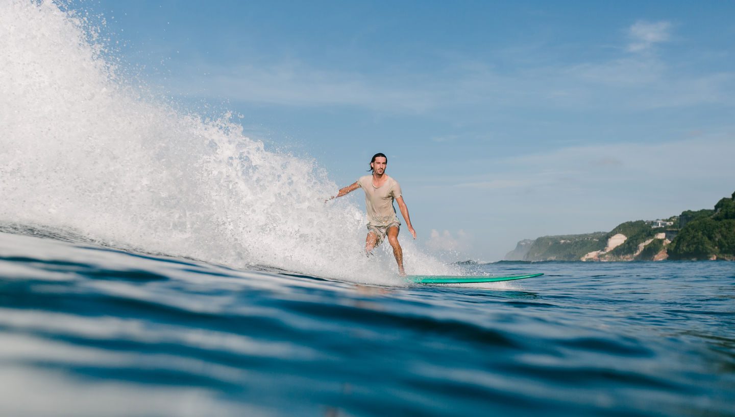 side view of young man in wet t-shirt riding waves on surfboard while having vacation