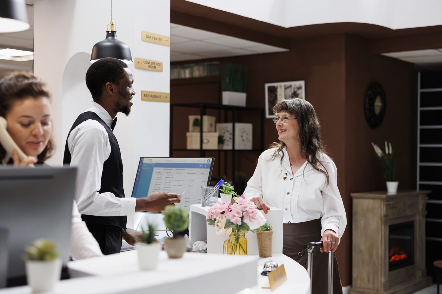 Senior woman at front desk assisted by employee with check-in, verifying identification in hotel reception. Male concierge completes registration process for elderly female traveler with her passport.