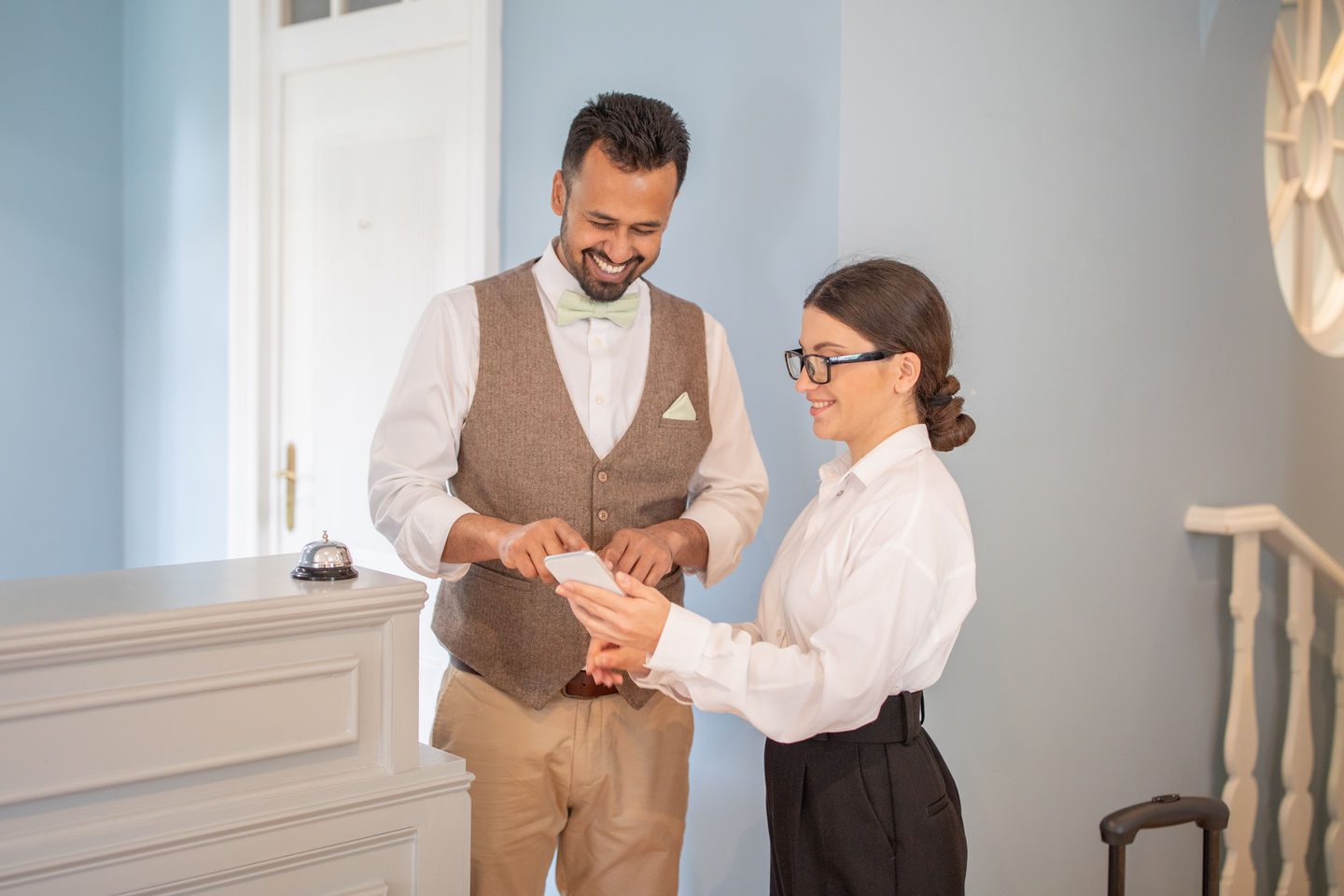 A smiling hotel receptionist assists a guest with their check-in process at an inviting boutique hotel during the day, showcasing a warm hospitality experience.
